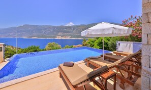 A pool with a view of the sea, lounge chairs, and a white umbrella. - Villa Nane (Kas)