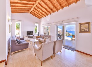 A spacious living room with a wooden ceiling, a sofa, a coffee table, and a television. - Villa Nane (Kas)