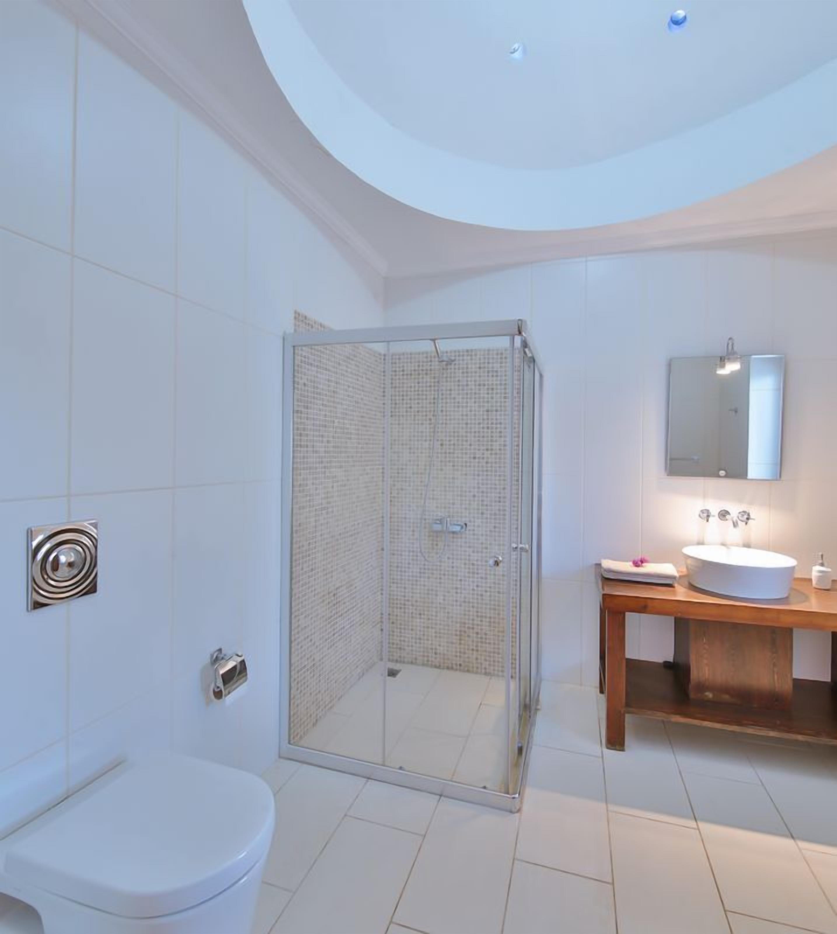 Une salle de bain moderne dotée d’une douche à parois de verre, de toilettes blanches et d’un meuble-lavabo en bois avec un évier et un miroir.
