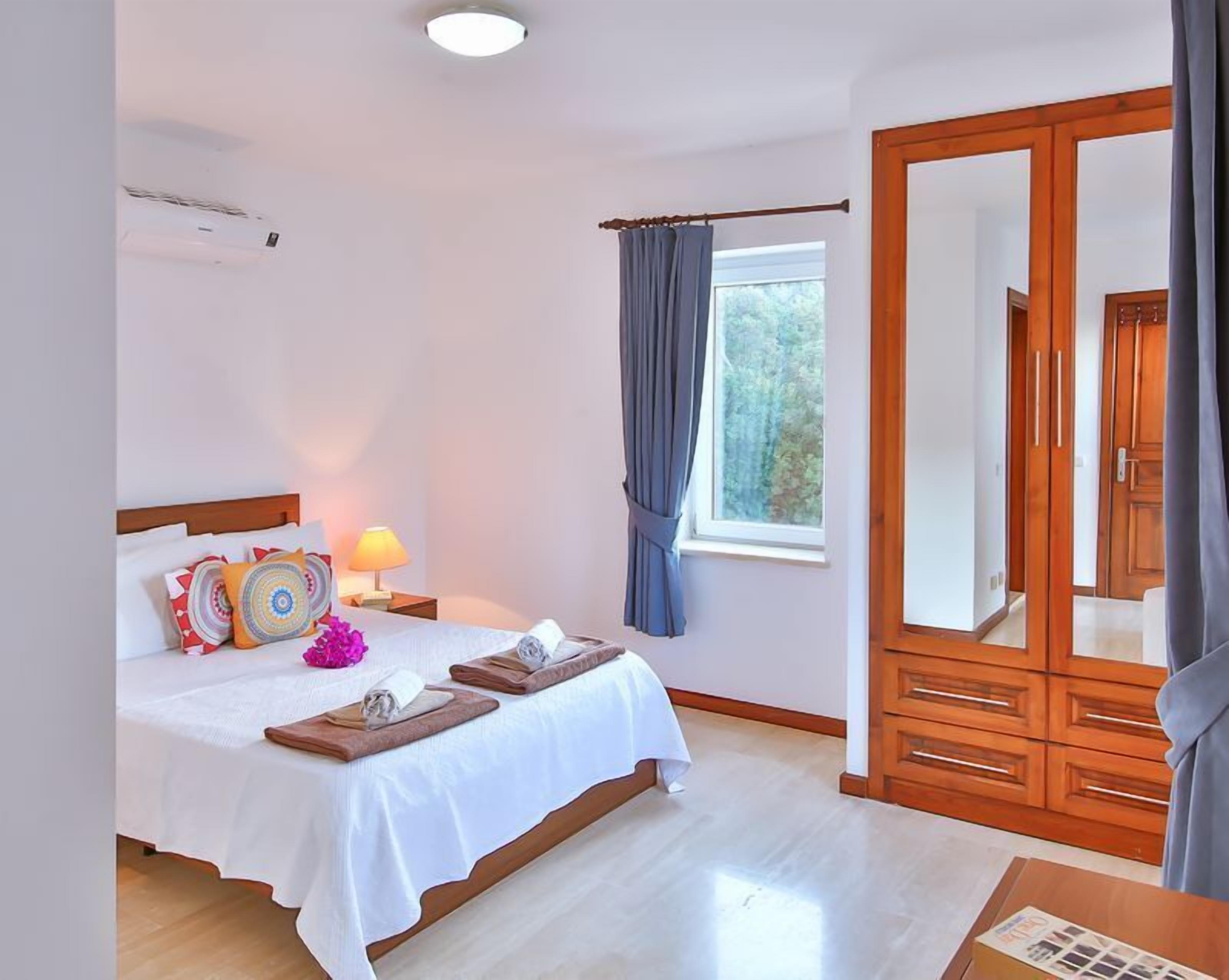 A hotel room with a bed, bedside table, lamp, and a large mirror.