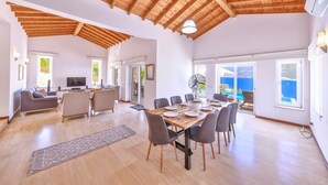 Un espai saló ampli amb sostre de fusta, taula de dinar preparada per a sis i vista al mar a través de grans finestres.