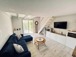 Una sala de estar moderna con un sofá azul, una mesa de centro de madera y un televisor montado en la pared.