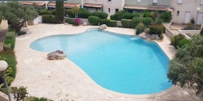 Una piscina rodeada de vegetación y un edificio con techo de tejas.