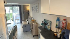 A compact kitchen with a dining area, a small side table, and a view of the outside. - Valras-Loc – Petite maison avec jardin et piscine (Valras-Plage)