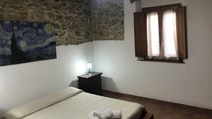 A bedroom with a bed, a nightstand, a ceiling fan, a window with curtains, and a wall with a painting.
