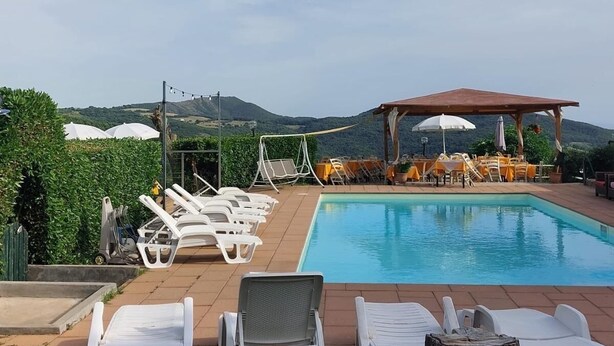 A pool area with lounge chairs and umbrellas, surrounded by greenery and hills.