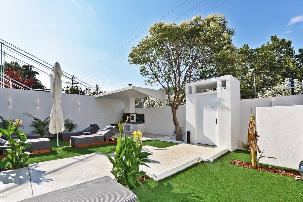 Eine moderne Außenpatio mit Kunstgrasanlage, Sitzbereichen und einer weißen Wand.