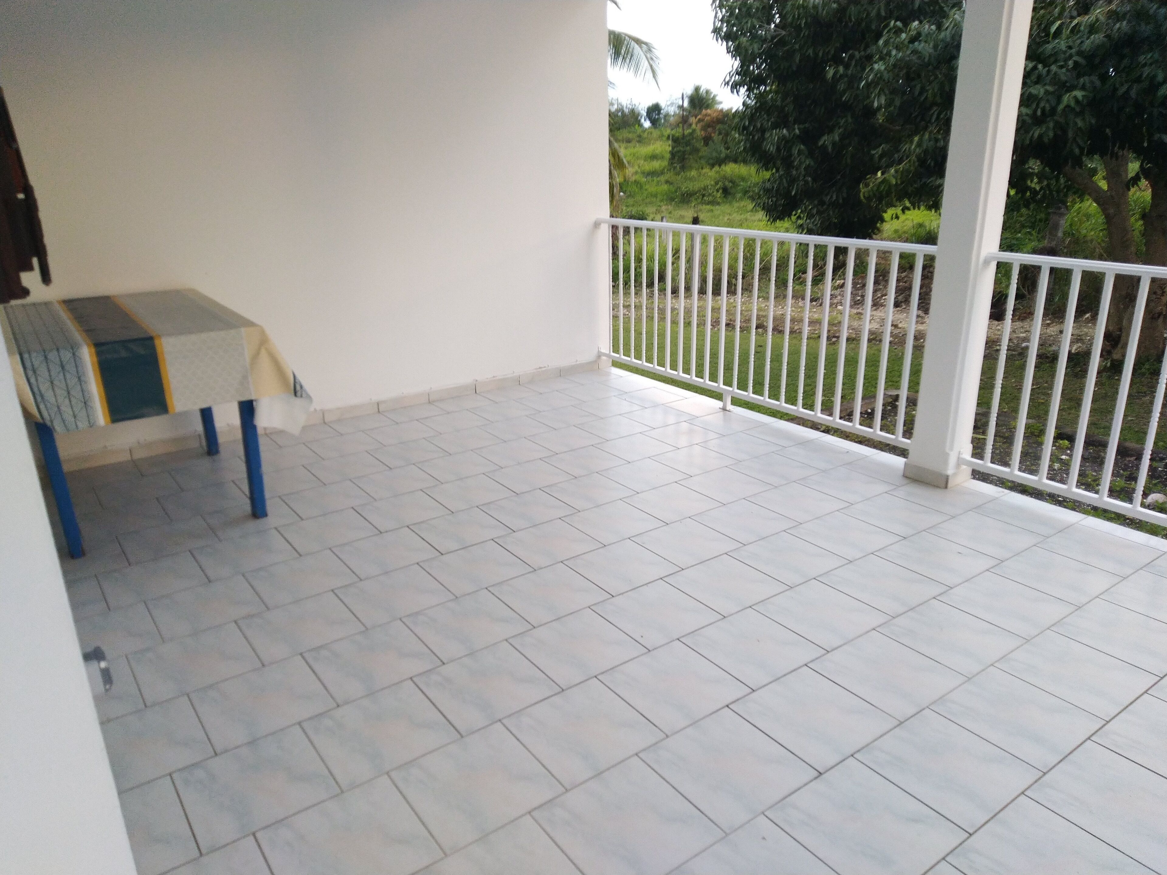 Een balkon met een betegelde vloer, een tafel met een tafelkleed en een witte reling.