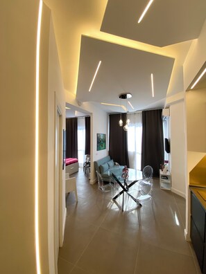 A modern living room with a glass dining table, clear chairs, a sofa, and a TV mounted on the wall. - La Maison, a great apartment near the Colosseum! (Roma)