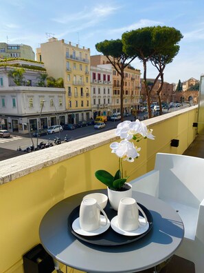 A balcony with a table set for two, a potted orchid, and a view of the cityscape. - La Maison, a great apartment near the Colosseum! (Roma)