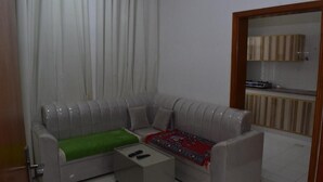Una sala de estar con un sofá gris, una mesita de centro y una cocina visible a través de un vidrio.