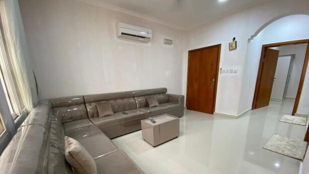 Una sala moderna con un amplio sofá seccional, una mesita de centro y una puerta que da a otra habitación.