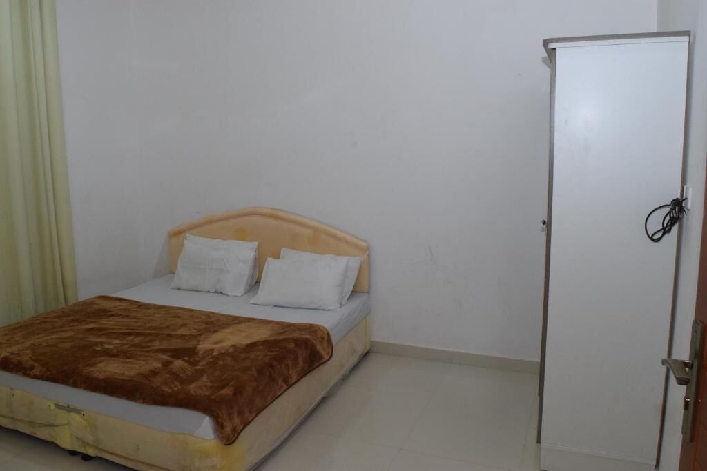 A single bed with a wooden headboard, a brown blanket, and white pillows. There is a white wardrobe to the right.