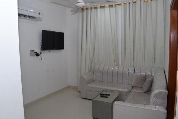 Un salon avec un canapé blanc, une petite table basse, un téléviseur fixé au mur et un ventilateur de plafond.
