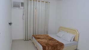 Una habitación pequeña y limpia con una cama, una ventana con cortinas y un equipo de aire acondicionado en la pared.