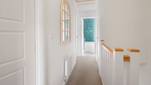 Un couloir aux murs blancs, avec un plafond en bois, et une vue sur une pièce dont un mur est recouvert de carreaux verts.