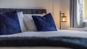 Un lit bien fait, avec des oreillers bleus et blancs, une tête de lit sombre et un luminaire fixé au mur.