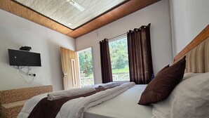 A bedroom with a bed, a television mounted on the wall, and a window with curtains. - Namami Kedara Resort (Ukhimath)