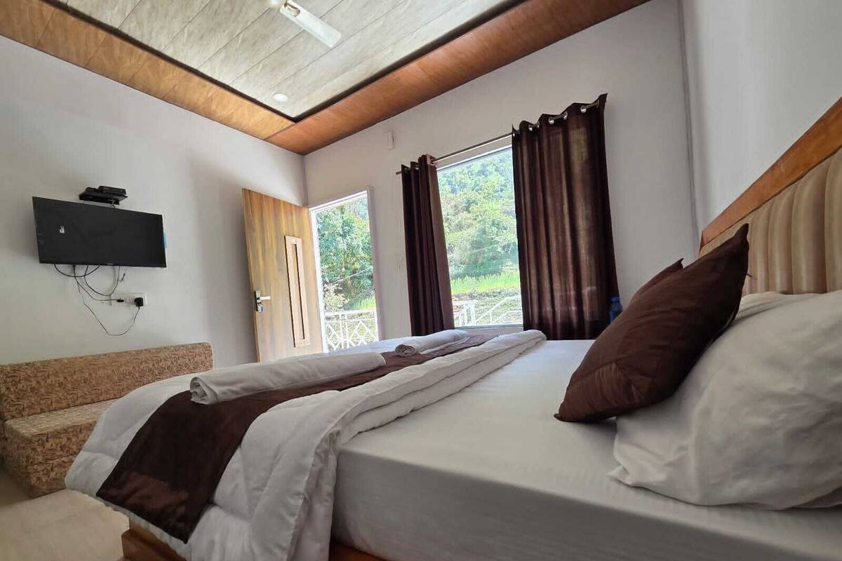 A bedroom with a bed, a television mounted on the wall, and a window with curtains.