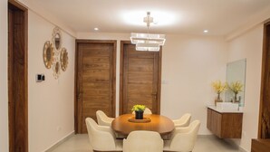 A dining area with a round table, six chairs, a chandelier, wooden doors, a mirror, and a small plant. - little hideaway (Dar es Salaam)