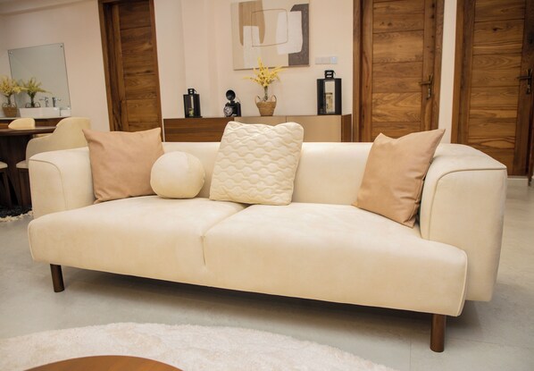 A beige sofa with three pillows, a white rug, wooden doors, and a wall-mounted mirror.