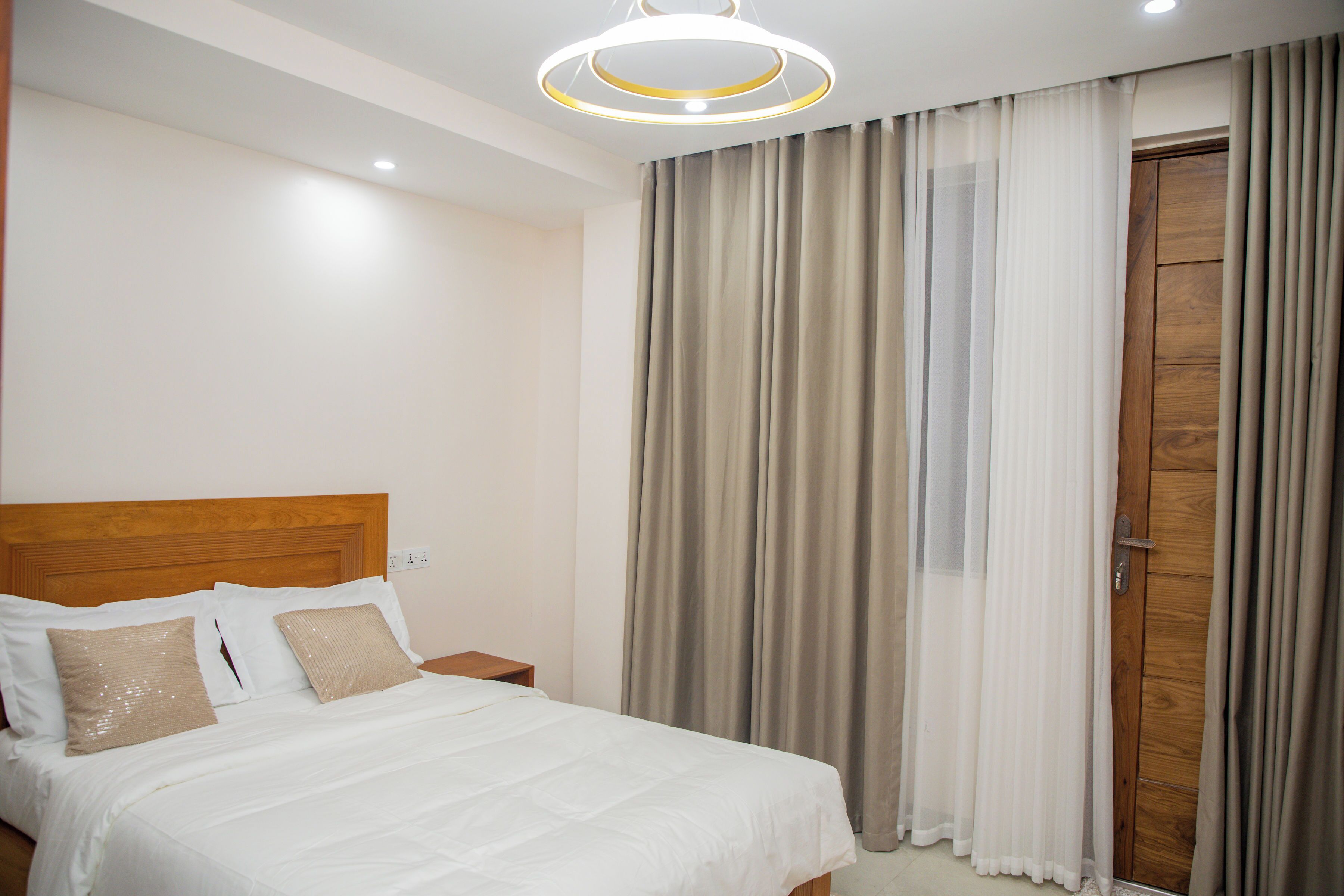 Un letto rifatto con lenzuola bianche e cuscini color beige, una testiera in legno e un comodino con una lampada.