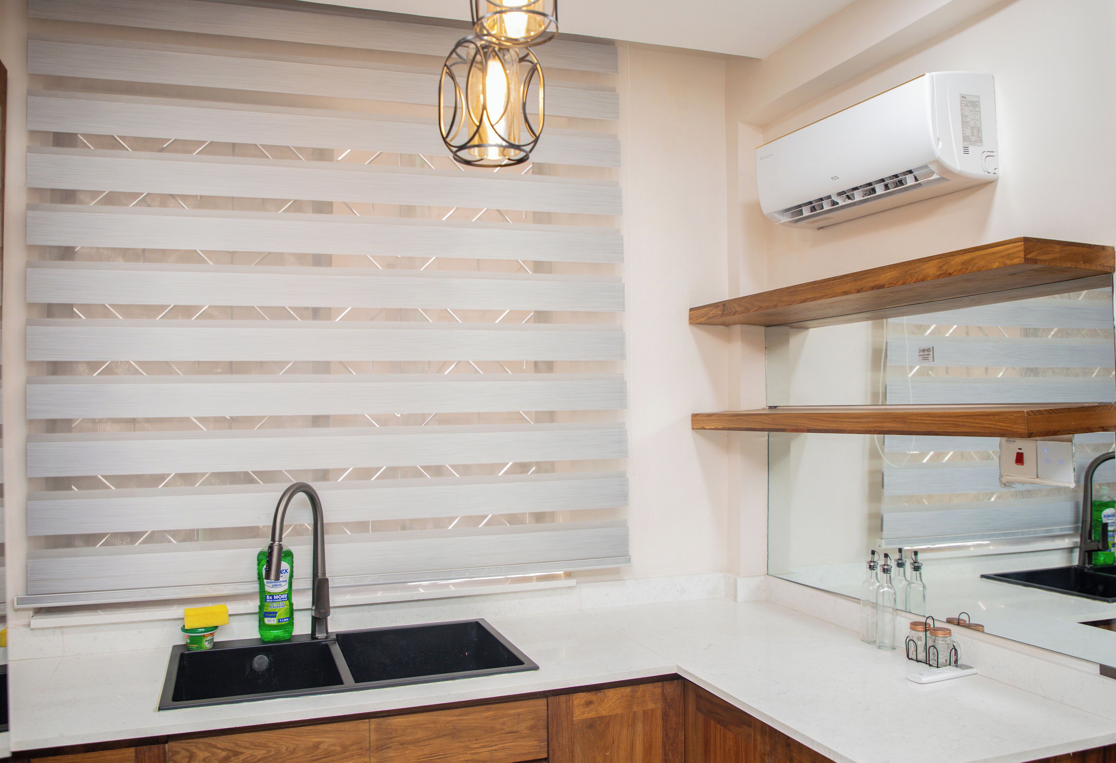 A modern kitchen with a built-in sink, a window with blinds, a pendant light, and an air conditioning unit.