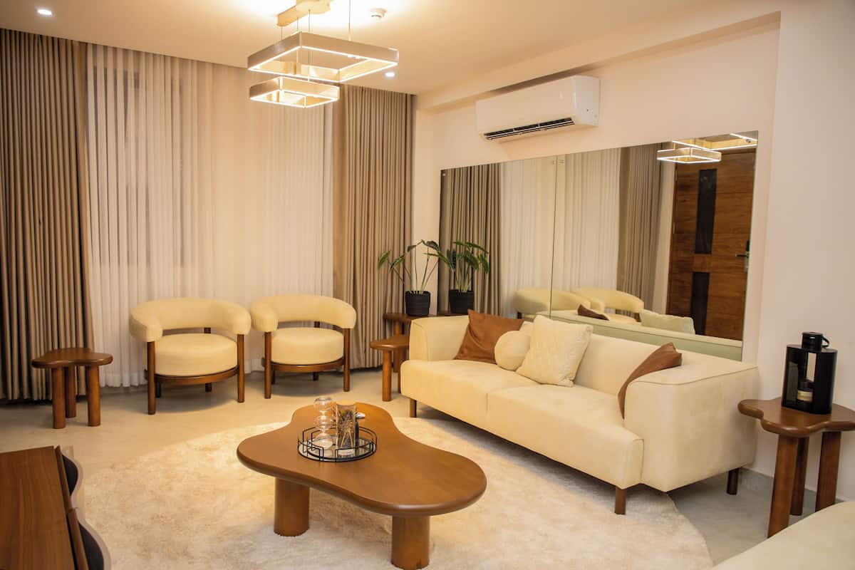 A modern living room with a beige sofa, two armchairs, a coffee table, and a wooden side table.
