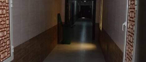 Un pasillo con paredes y piso de baldosas, que conduce a una puerta oscura.