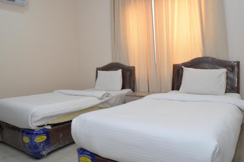 A hotel room with two single beds, a window with curtains, and a wall-mounted air conditioner.