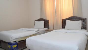 A hotel room with two single beds, a window with curtains, and a wall-mounted air conditioner.