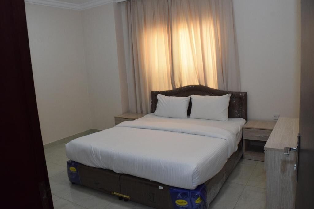 A hotel room with a bed, a nightstand, a wooden headboard, and a curtain.