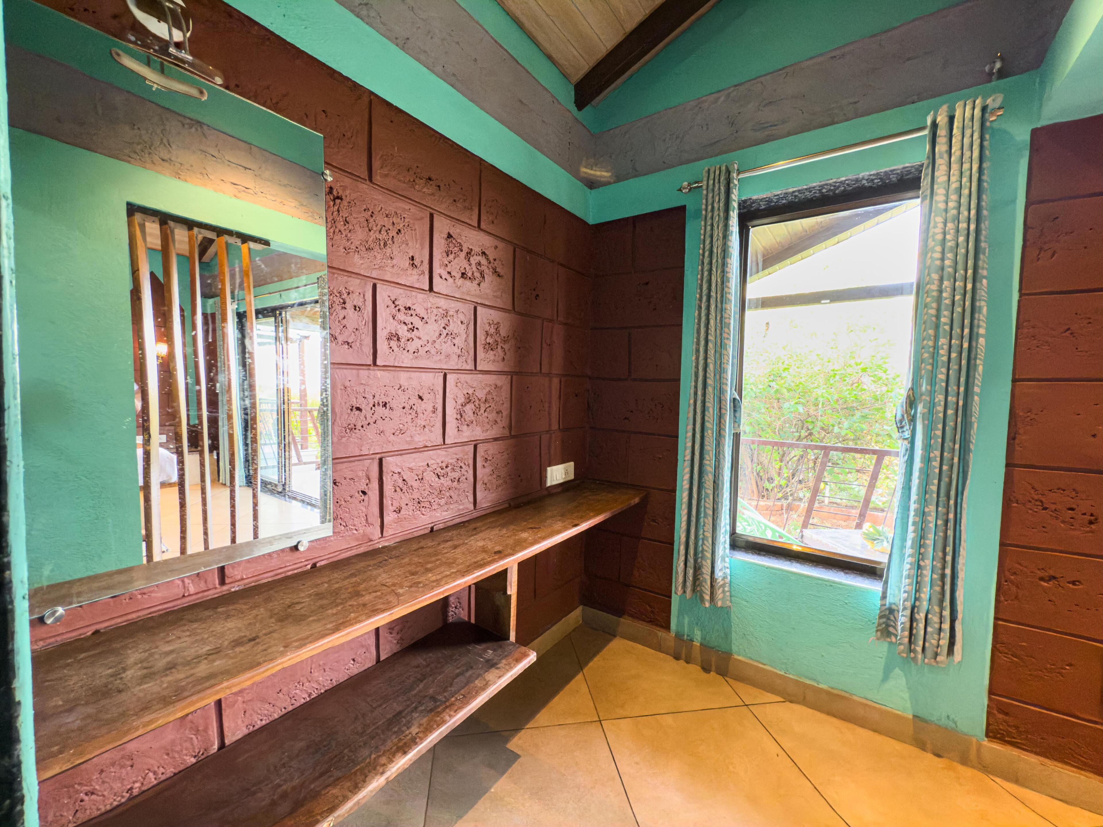 A room with a wooden bench, a window with curtains, and a view of greenery outside.