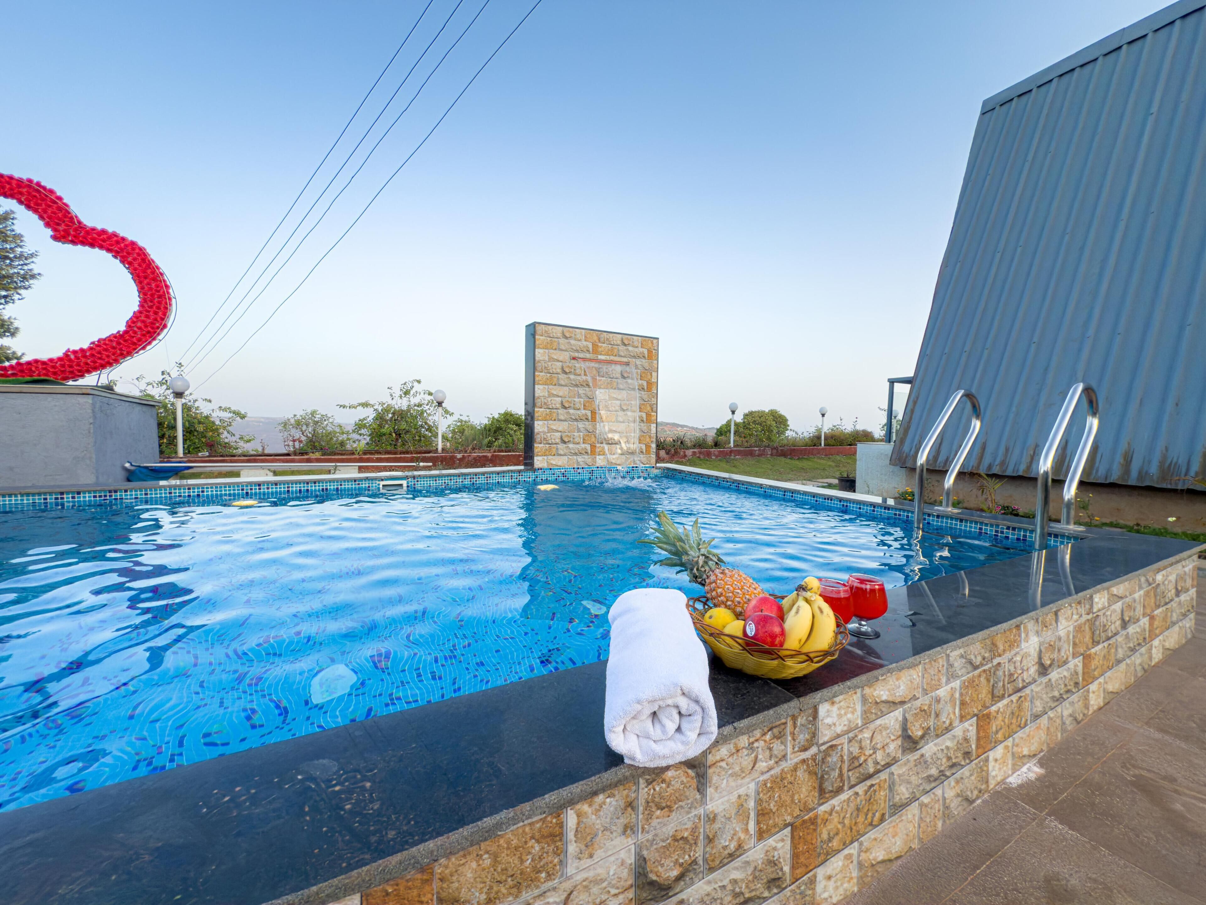 Una piscina amb una paret de pedra, una tovallola i una cistella de fruita.
