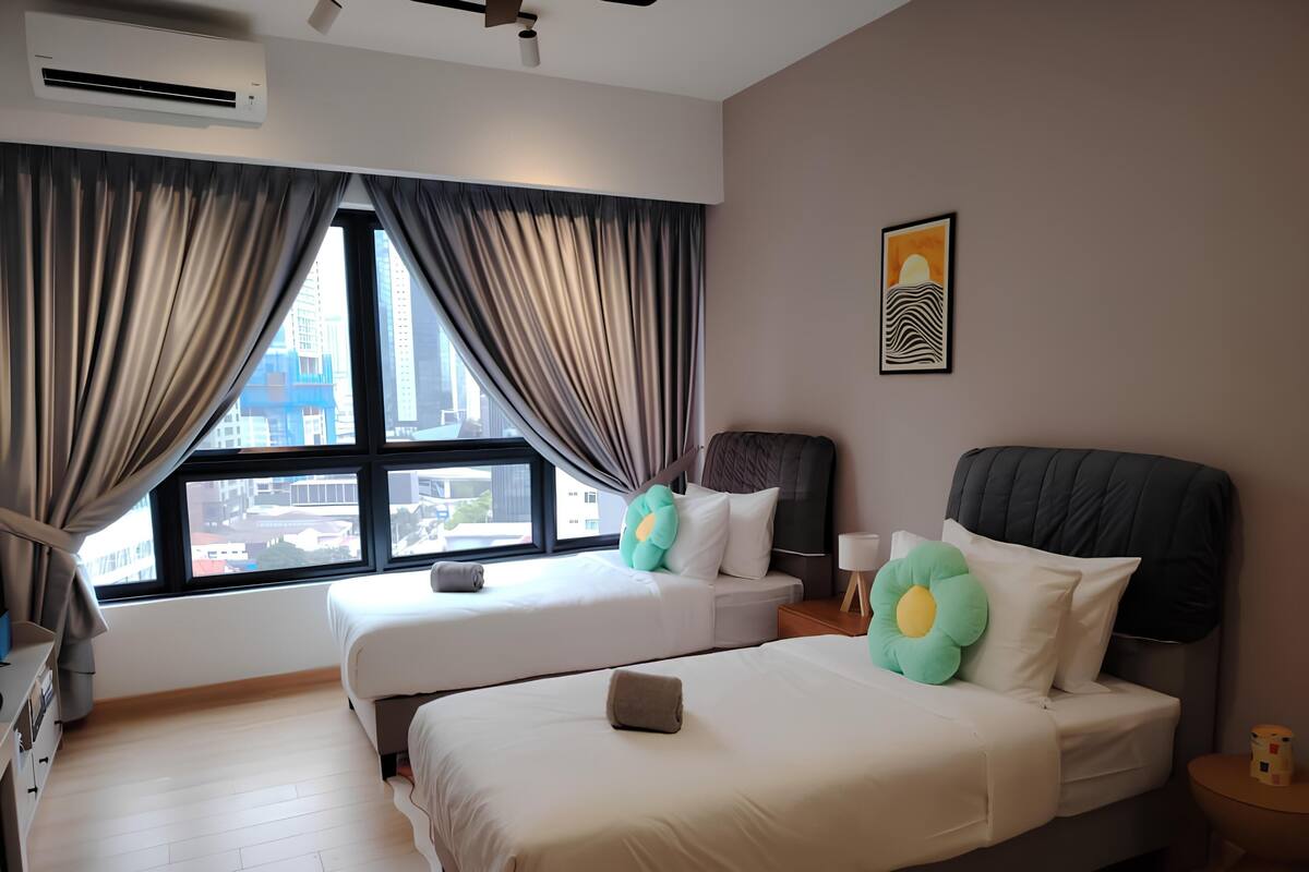 A hotel room with two beds, a large window with curtains, a ceiling fan, and a city view.