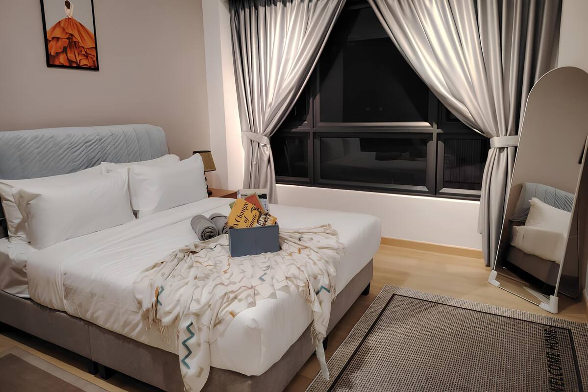A modern hotel room with a large bed, a bedside table with a lamp, and a window with curtains.
