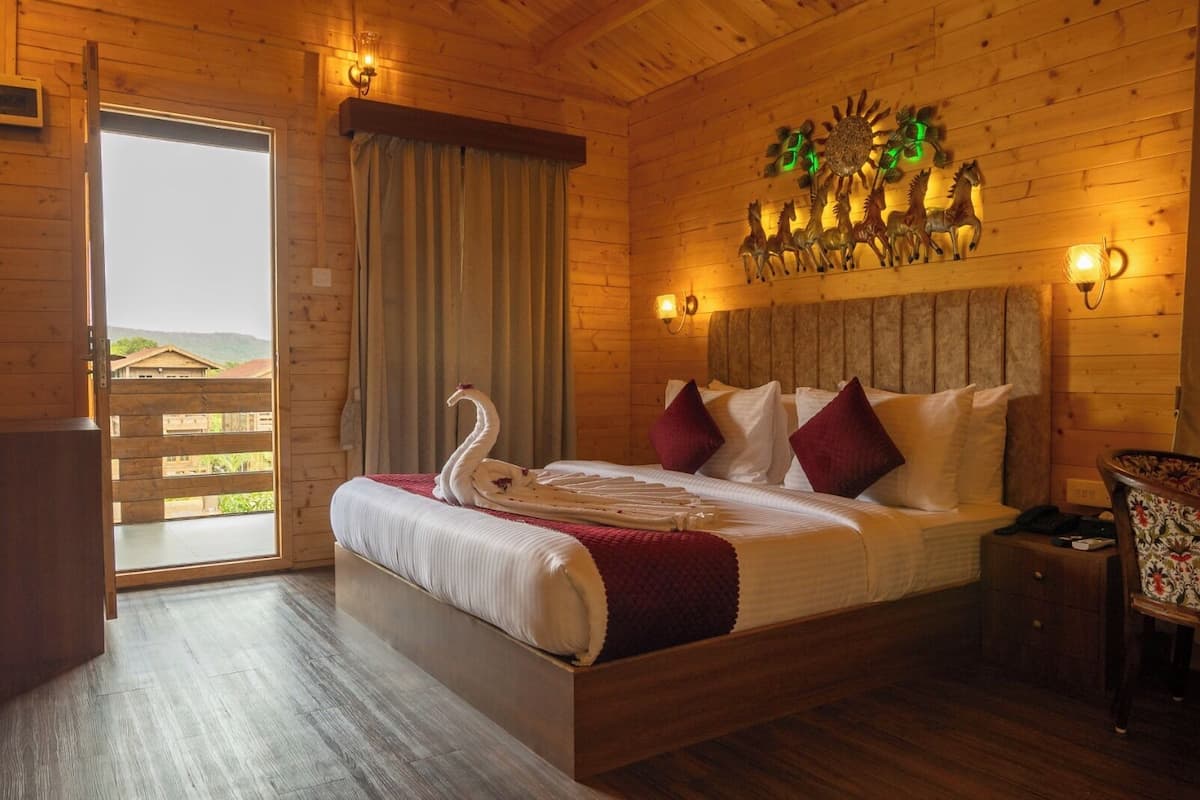 A wooden cabin-style bedroom with a bed, pillows, a swan decoration, a wall-mounted sun decoration, and a view through a door.