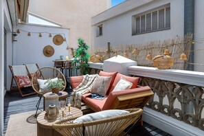 A cozy outdoor seating area with wicker furniture, a cushioned sofa, and a small table with drinks and decorative items. - Genteel Home Mitjana Terrace (Málaga)