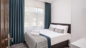 A hotel room with a bed, a nightstand, a desk, and a window with curtains.