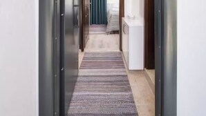 A hallway with a patterned rug, a number '3' sign, a door leading to a room with a bed and a blue curtain, and a white cabinet.