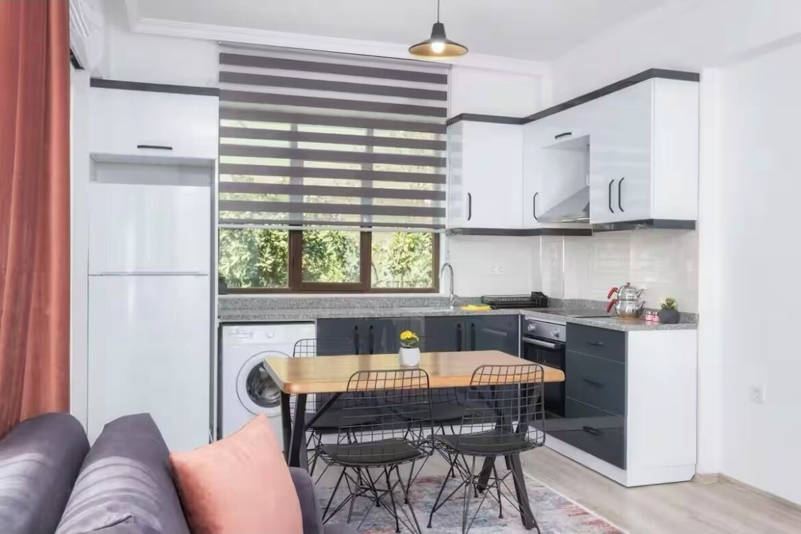 A compact kitchen with a dining area, a washing machine, and a sofa with cushions.