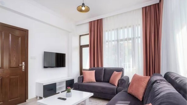 A modern living room with a grey sofa, a white coffee table, and a mounted TV.