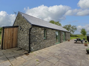 A stone building with a sloped roof, a wooden door, and a patio area with a picnic table. - Cwtch (Tregaron)