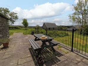A picnic table with a hat and shoes, a stone pathway, and a fenced area with a view of houses and greenery. - Cwtch (Tregaron)