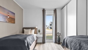 Ein Hotelzimmer mit zwei Betten, einem Nachttisch, einer Lampe, einem Blumentopf und Blick auf eine Wohngegend.