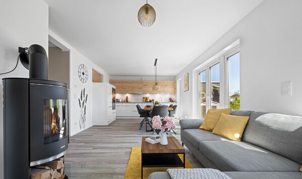 A modern living room with a fireplace, a sofa, a coffee table, and a dining area in the background. - Vier Jahreszeiten - Terrace, Infrared Sauna, Washing Machine, Parking Space (Olpenitz)