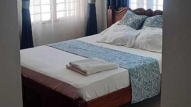 A bedroom with a bed, curtains, a ceiling fan, and a window. - Lux Suites Shiv Apartments Nyali Cinemax (Mombasa)
