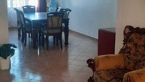 A spacious living area with a dining table and chairs, a patterned armchair, and a ceiling fan. - Lux Suites Shiv Apartments Nyali Cinemax (Mombasa)