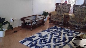 A living room with a flat-screen TV mounted on the wall, a coffee table, two sofas, a patterned rug, and a window with curtains. - Lux Suites Shiv Apartments Nyali Cinemax (Mombasa)