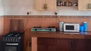 A kitchen with wooden cabinets, a gas stove, a microwave, and a countertop with a few items. - Lux Suites Shiv Apartments Nyali Cinemax (Mombasa)